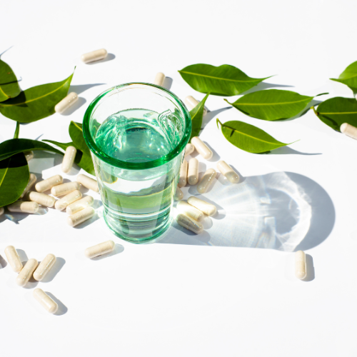 Glass cup with water and capsules and pills on a white background. Green leaves The topic of nutraceuticals and supplementation. Alternative Medicine Copy space for text